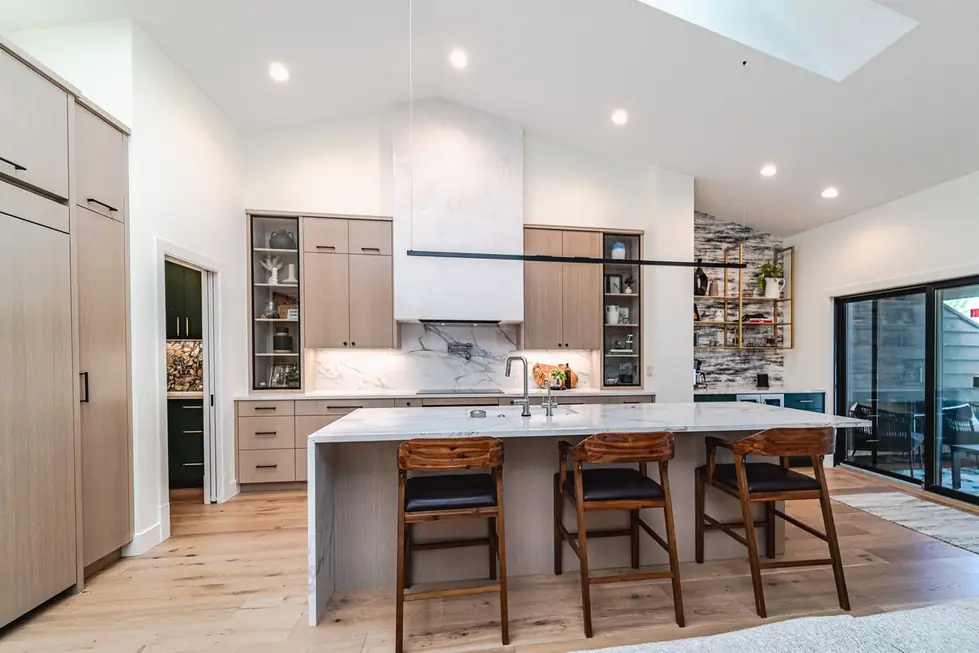 Vaulted Avid Builders kitchen remodel with a marble hood surround, pale cabinetry and wooden stools at the island